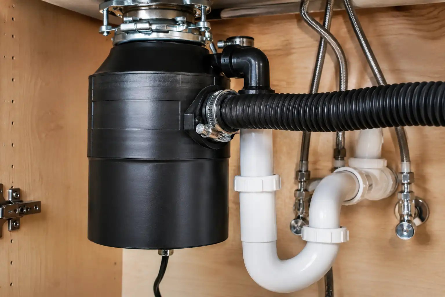 Under-sink view of a ribbed dishwasher drain hose connected to the inlet knockout port of a garbage disposal.