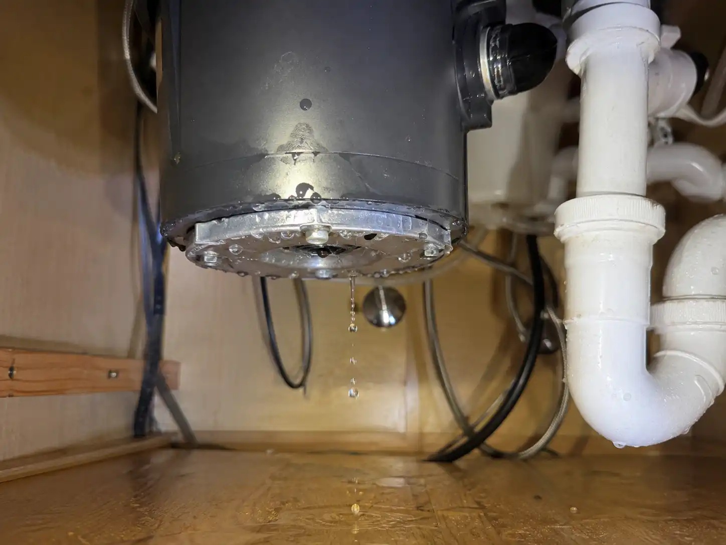 Water dripping from the lower motor housing of an under-sink garbage disposal unit onto a cabinet floor.